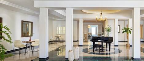 A spacious lobby with a grand piano, white columns, and a polished marble floor.