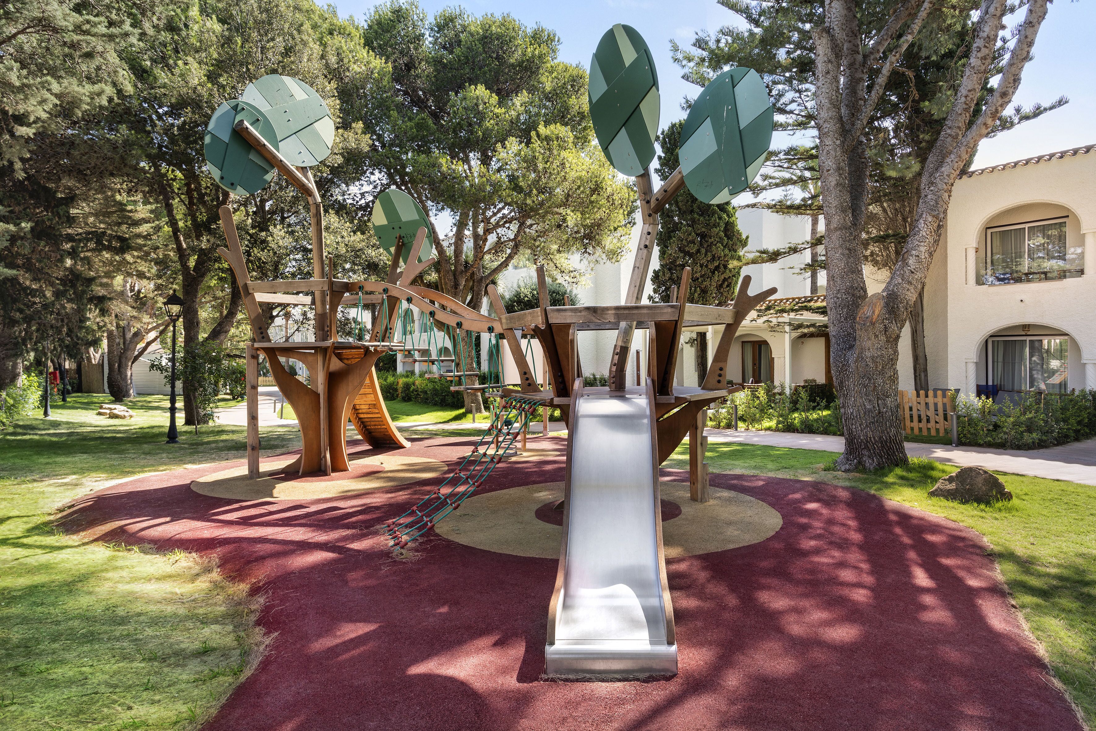 Un parque infantil con tobogán, estructuras para escalar y suelo de goma roja.