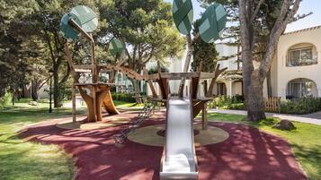Un parque infantil con tobogán, estructuras para escalar y suelo de goma roja.