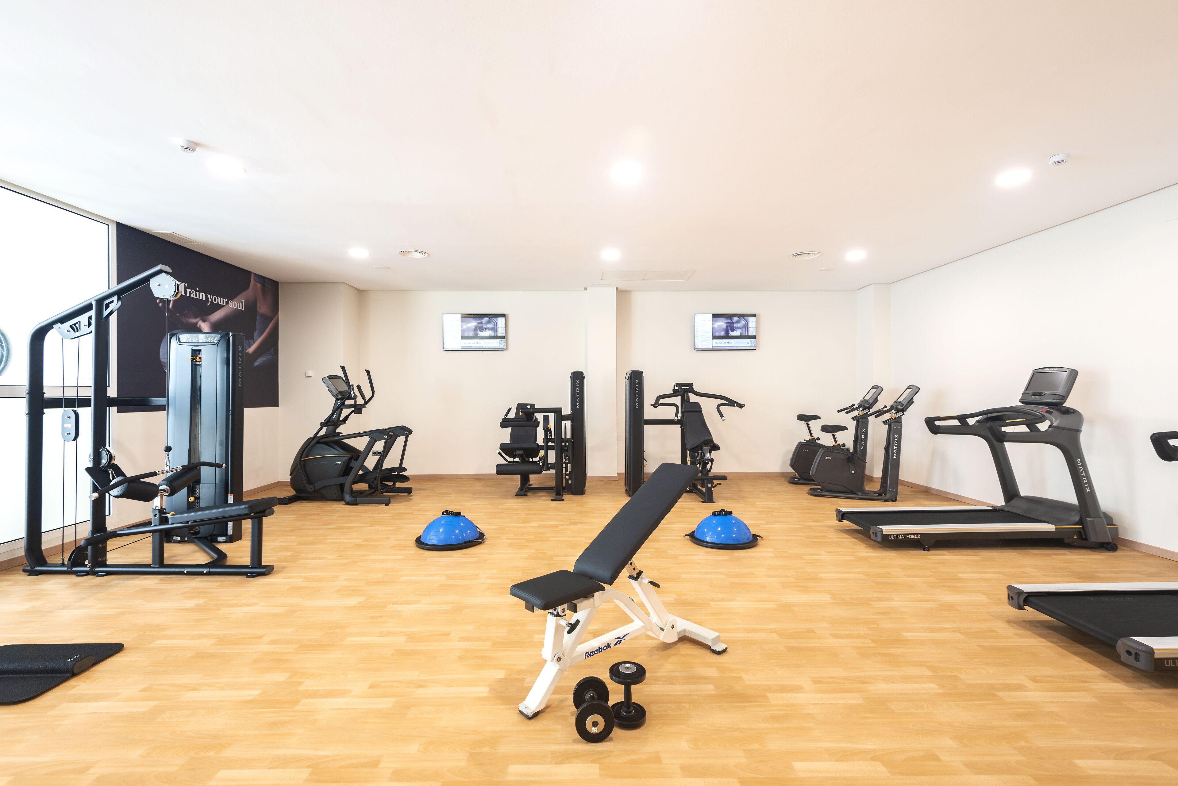 Un gimnasio con equipamiento de ejercicio como cintas de correr, elípticas y bancos de pesas.
