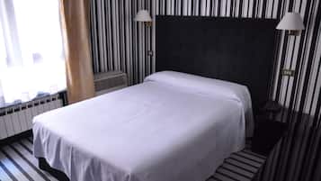 A hotel room with a large bed, striped wallpaper, and two wall-mounted lamps.