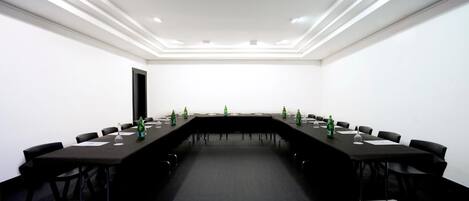 Uma sala de conferência com uma mesa comprida, cadeiras pretas e piso coberto por carpete.