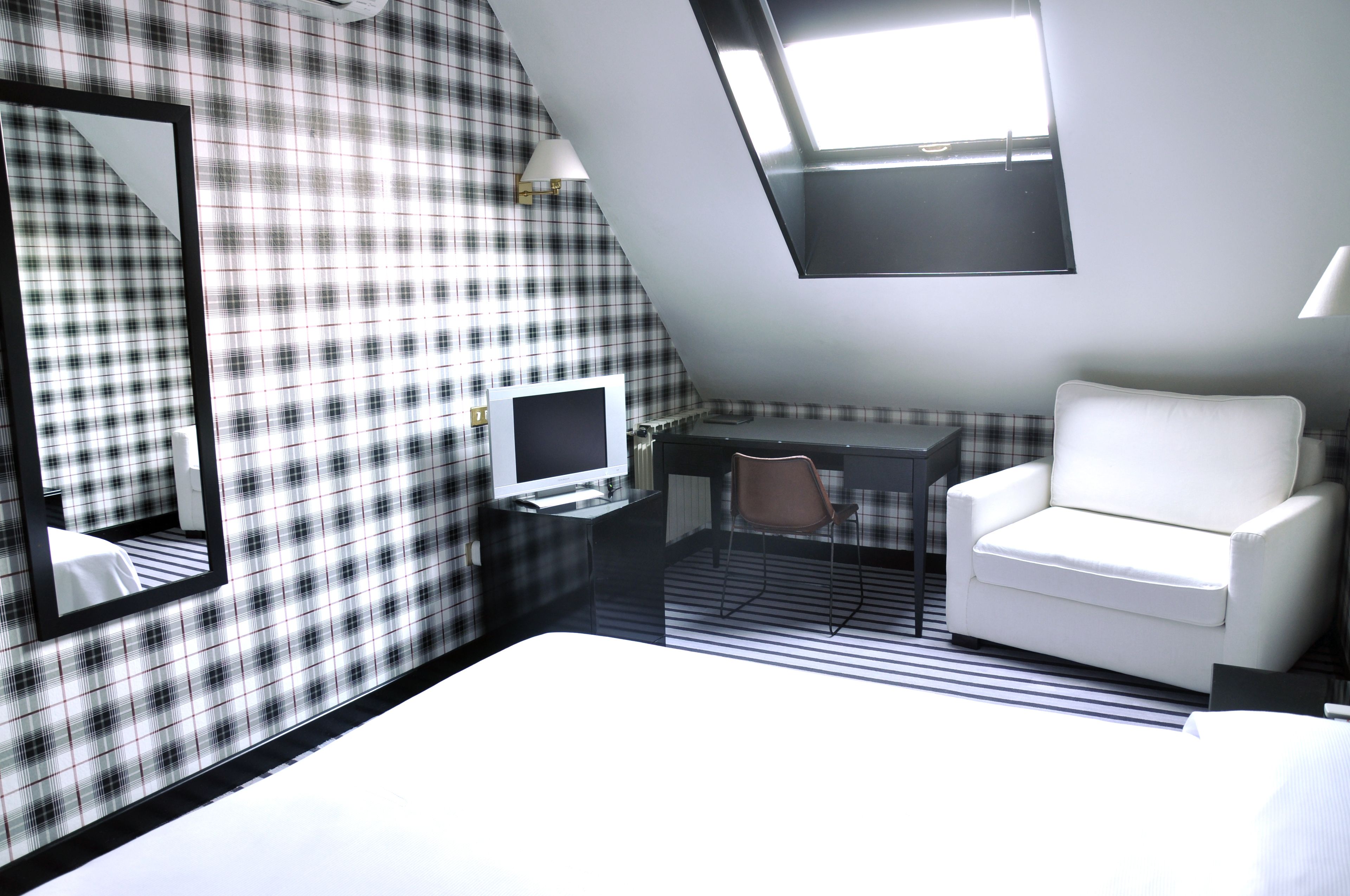 A hotel room with a bed, a desk, a chair, a TV, a mirror, and a window.