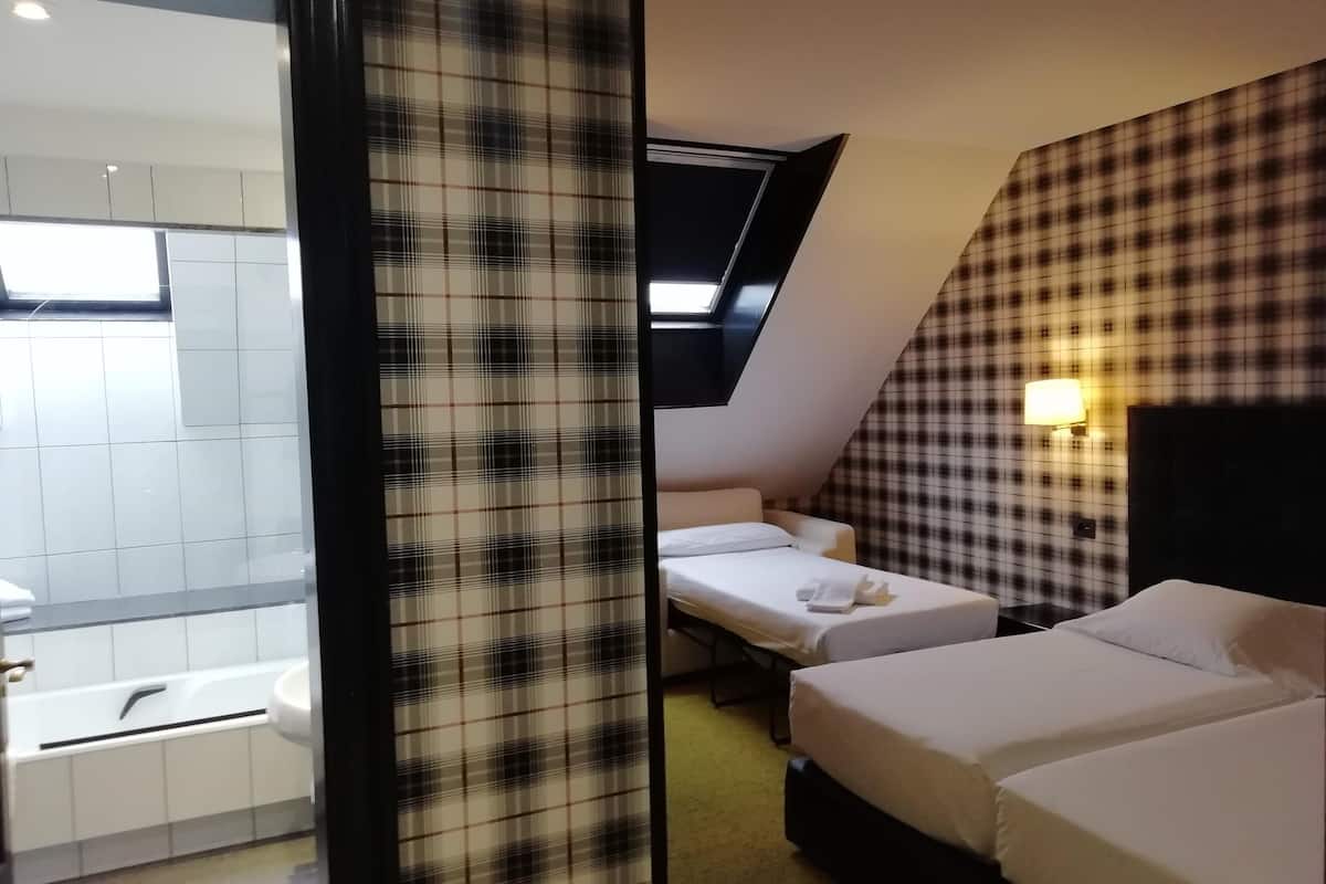 Quarto de hotel com duas camas, uma mesa pequena, um sofá, uma janela e banheiro com banheira e pia.