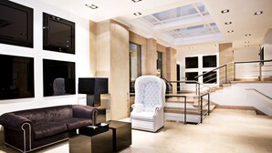 Eine moderne Hotelhalle mit hoher Decke, einer zentralen Treppe und einer Sitzecke mit Sofa und Sesseln.