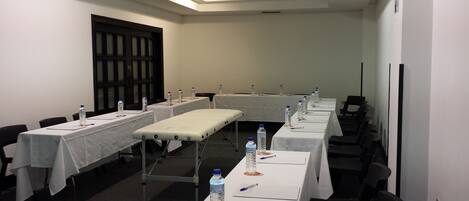 A conference room with long tables, chairs, water bottles, and a projector screen.