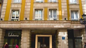 Ein mehrstöckiges Gebäude mit gelber Fassade, einem Eingang im Erdgeschoss mit der Aufschrift "Cafeteria" und einem Schild, das die Nummer "11" angibt.