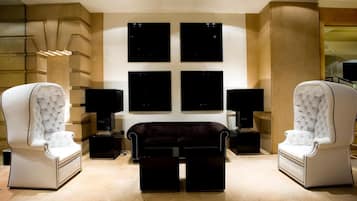 A modern living room with two white tufted armchairs, a dark sofa, and black side tables with lamps. There are four black framed artworks on the wall.