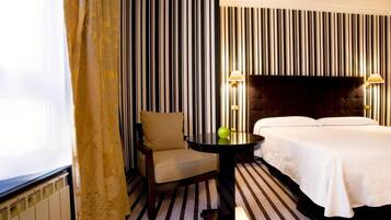 Ein Hotelzimmer mit gestreifter Tapete, einem Bett, einem Sessel und einem Tisch mit zwei Lampen.