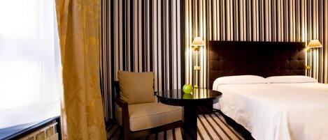 Una habitación de hotel con papel tapiz a rayas, una cama, una silla y una mesa con dos lámparas.