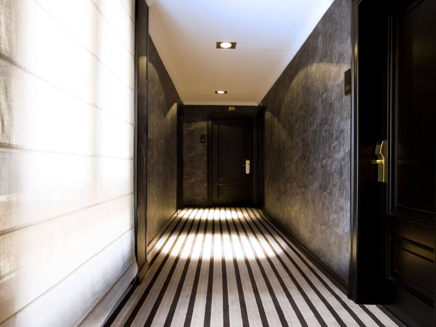 A narrow hallway with striped flooring, a dark door on the right, and a light source at the end.