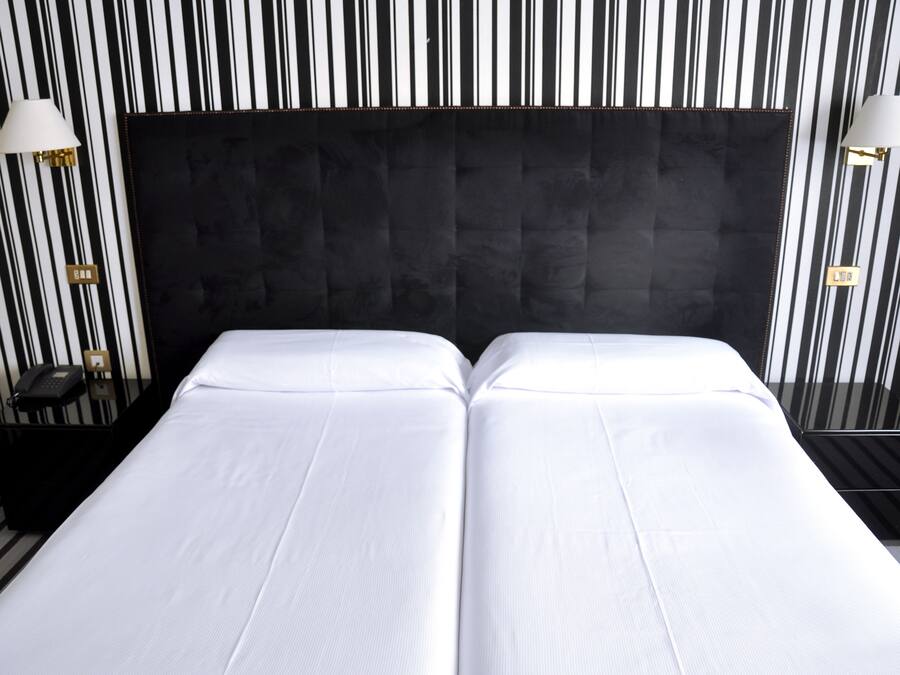 A hotel room with two beds, black headboard, striped wallpaper, and bedside lamps.
