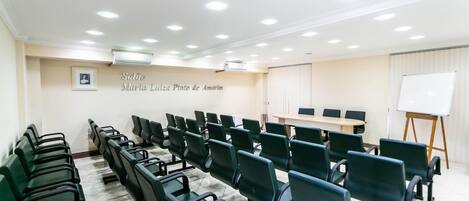 A conference room with rows of green chairs, a whiteboard, and a table.