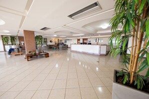 Un vestíbulo amplio con mostrador de recepción, zona de estar y plantas en macetas.
