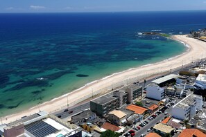 A coastal cityscape with a beach, buildings, and a road. - Portobello Pituba Praia (Salvador)