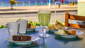 Una mesa con diversos platos y un vaso de bebida verde, con vista a una playa.