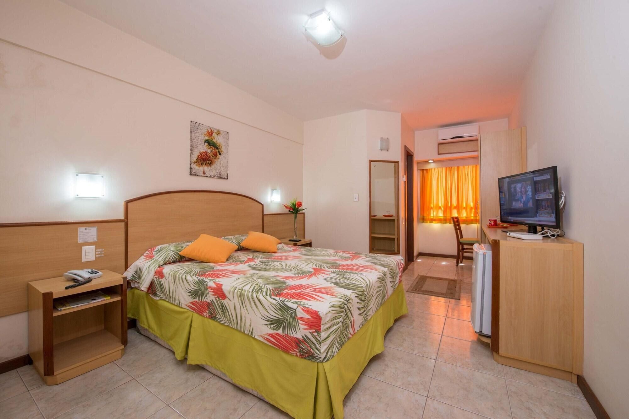 Una habitación de hotel con cama, escritorio, computadora, televisor y espejo.