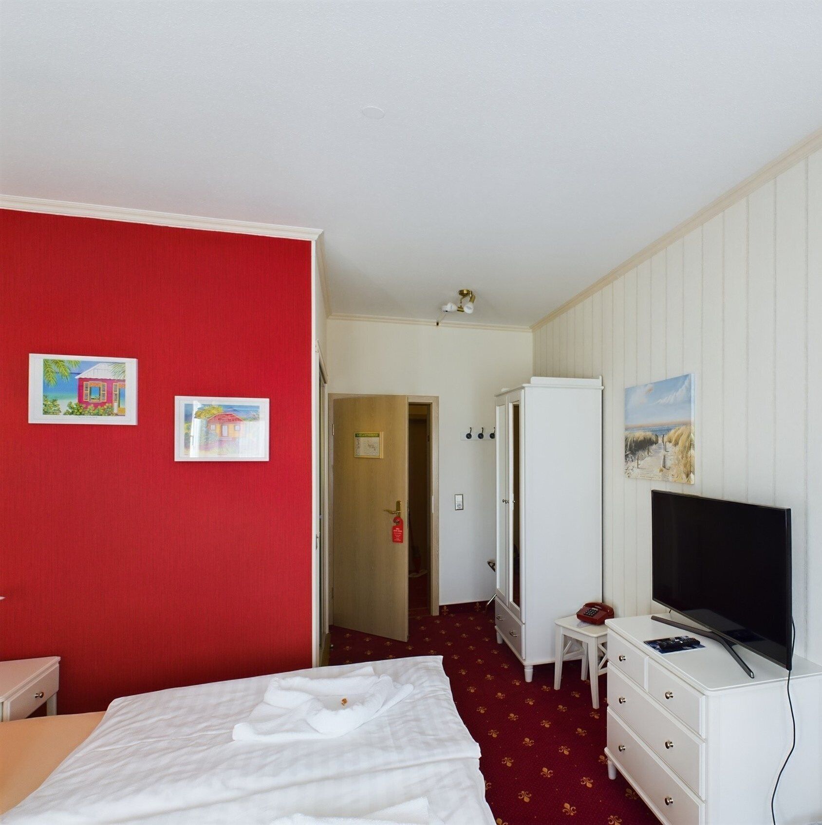 Una habitación de hotel con una cama, televisión, armario y dos cuadros en la pared.