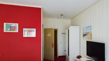 Una habitación de hotel con una cama, televisión, armario y dos cuadros en la pared.