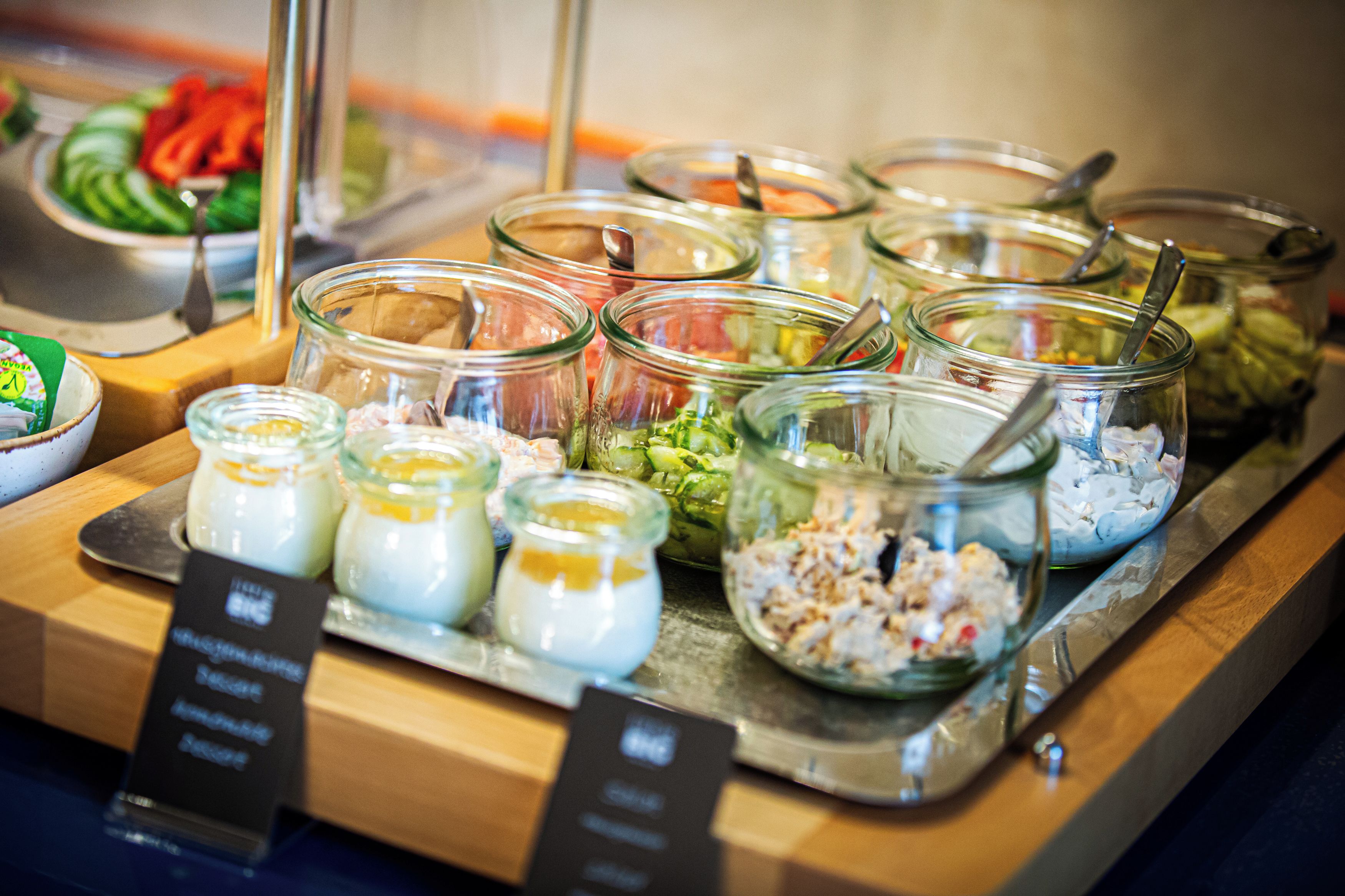 Un bufé con diversos alimentos en recipientes de vidrio, incluyendo ensaladas y salsas.