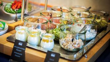 Un bufé con diversos alimentos en recipientes de vidrio, incluyendo ensaladas y salsas.