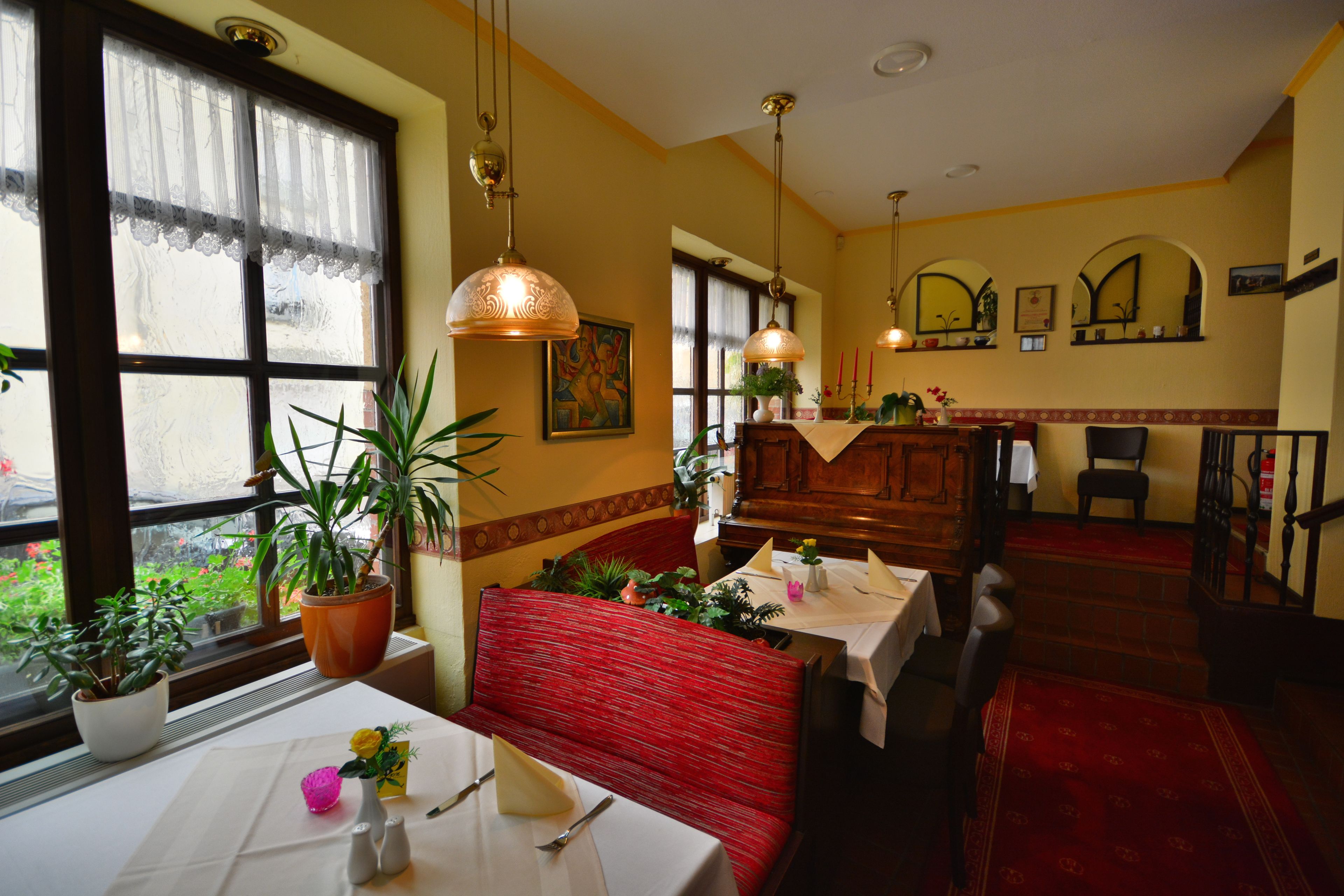 Un restaurant amb una barra amb seients tapissats de color vermell, una taula blanca amb un ram de flors i plantes en test.