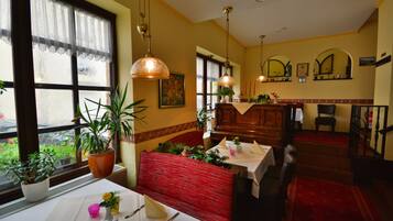 Ein Restaurant mit einer roten Sitzbank, einem weißen Tisch mit Blumen in einer Vase und Topfpflanzen.