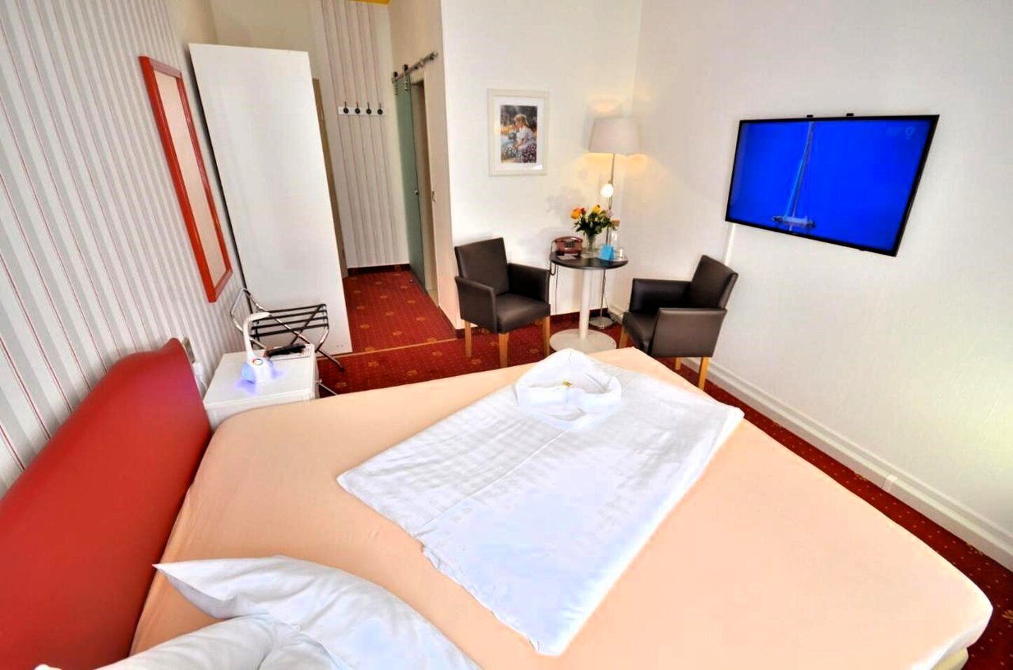 Ein Hotelzimmer mit einem Bett, einem Schreibtisch, zwei Stühlen, einem Fernseher und einer Tür zu einem anderen Raum.