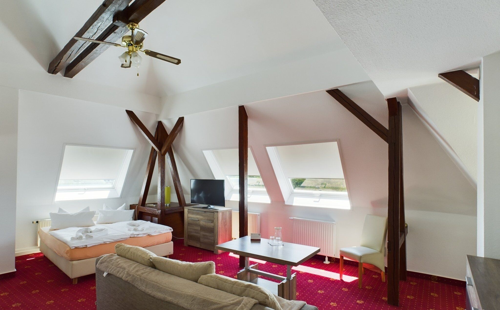 Ein Zimmer mit einem Bett, einem Schreibtisch, einem Sessel, einem Fernseher und einem Deckenventilator.