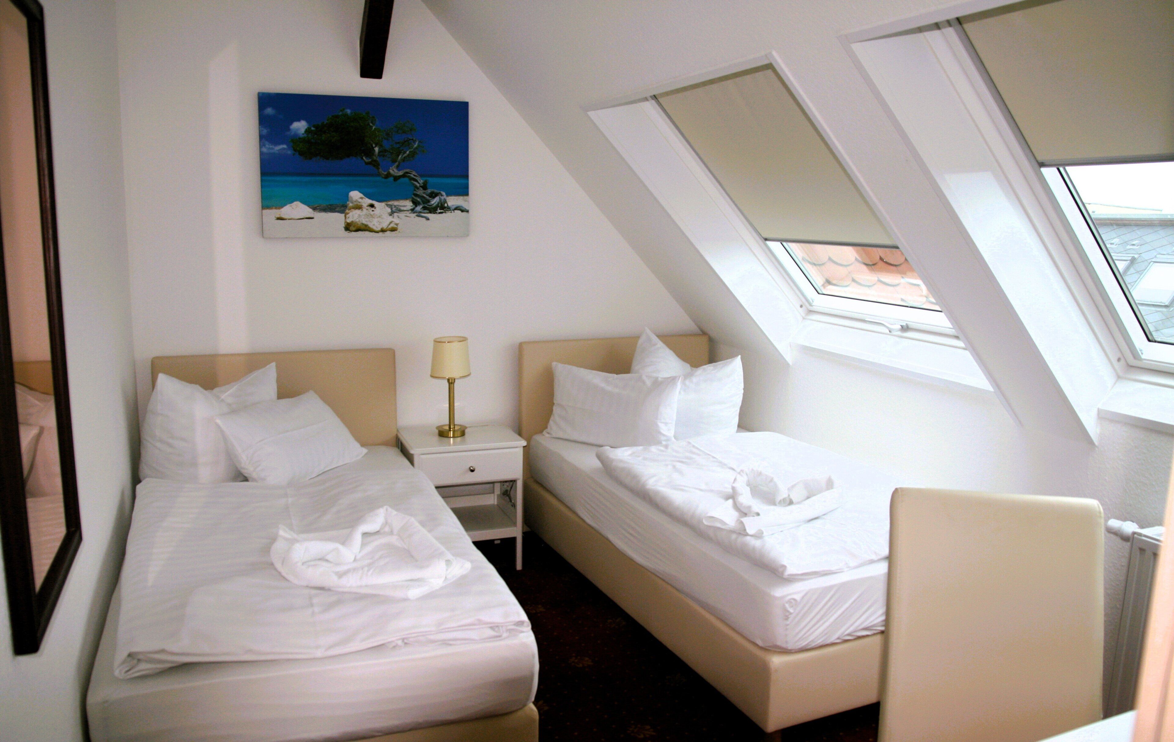 Een hotelkamer met twee bedden, een nachtkastje, een lamp, een schilderij van een strand en een dakraam.