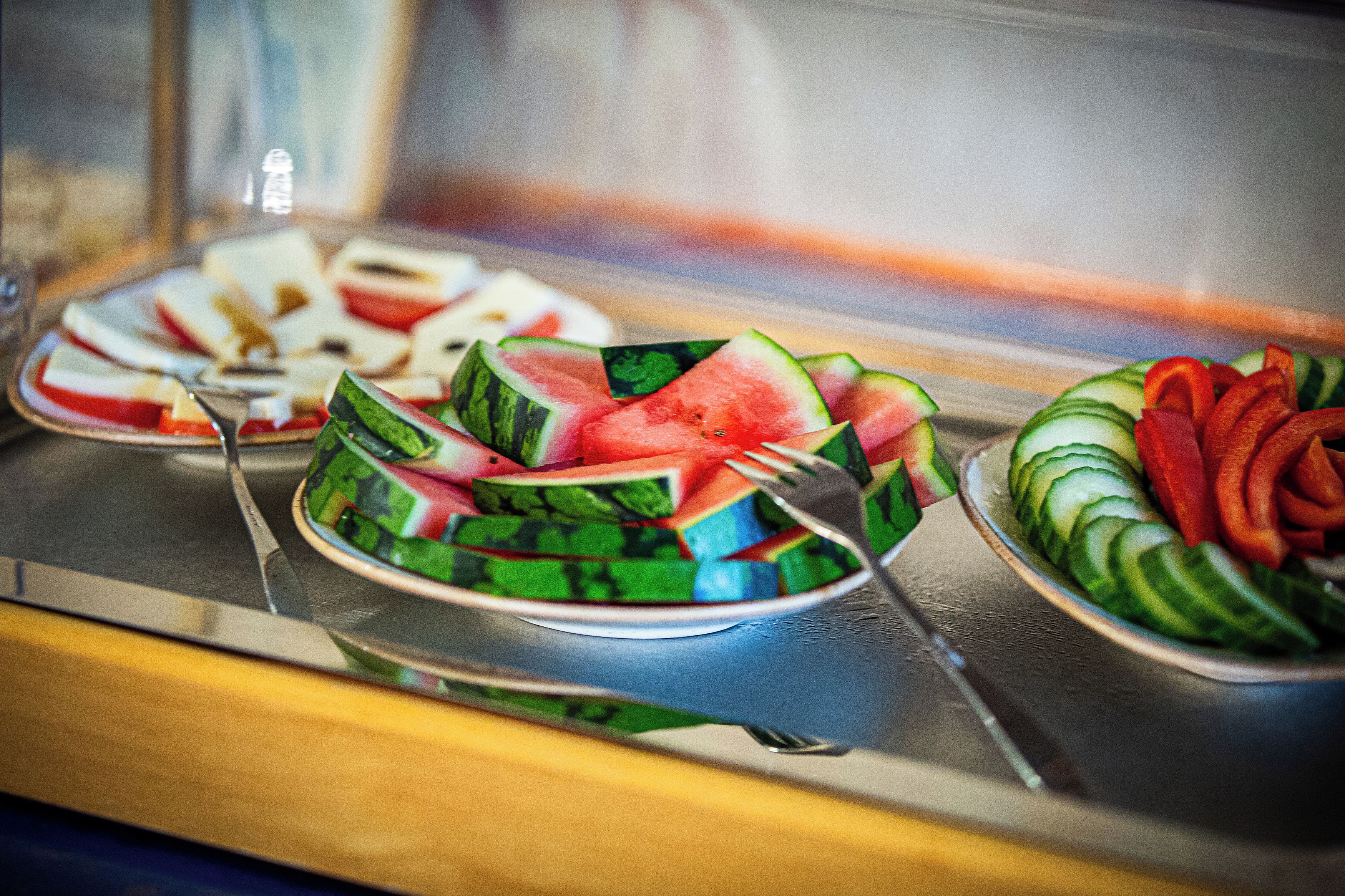 A buffet with plates of watermelon and cucumber slices.