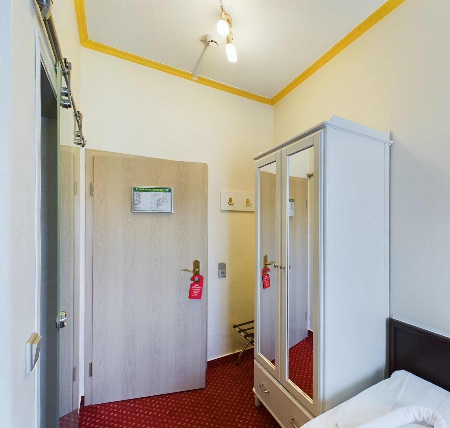 Une chambre d’hôtel avec un lit, une armoire, une porte avec une pancarte et un luminaire au plafond.