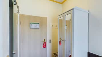 Ein Hotelzimmer mit einem Bett, einem Kleiderschrank, einer Tür mit einem Schild und einer Deckenleuchte.
