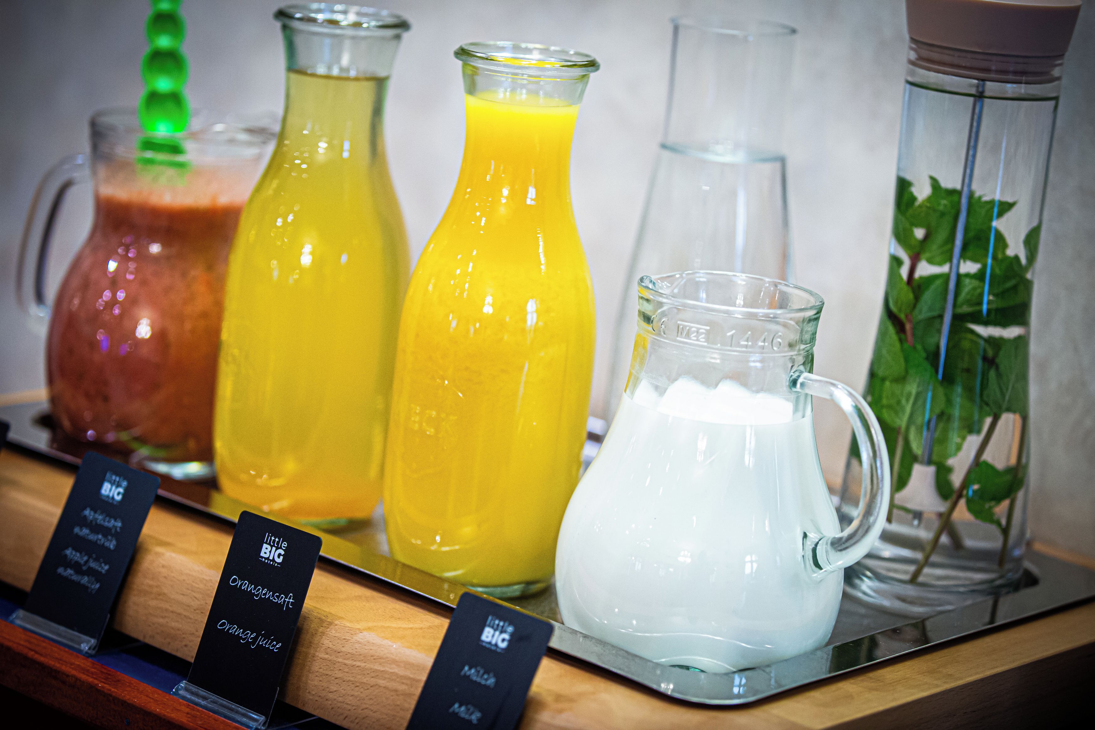 A selection of beverages including orange juice, a green drink, and a white beverage, served in various glass containers.