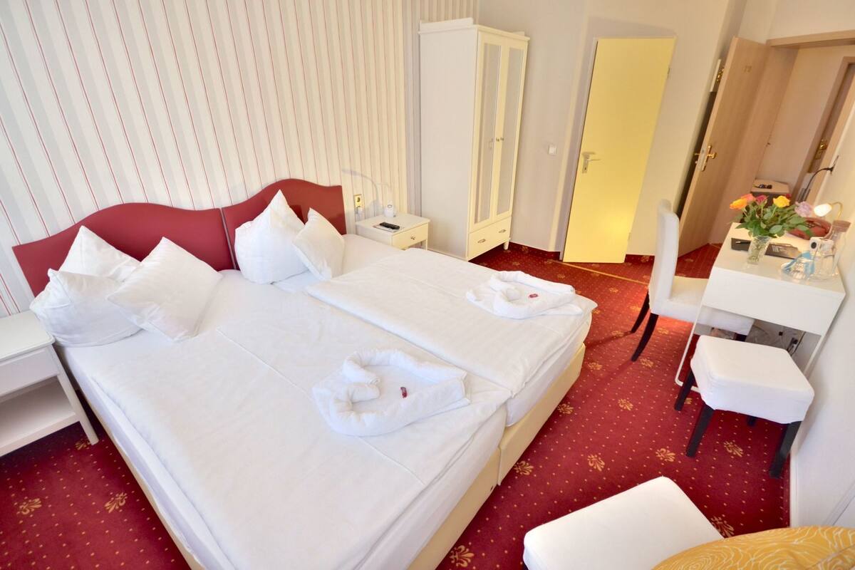 A hotel room with a large bed, a desk, a chair, and a wardrobe.