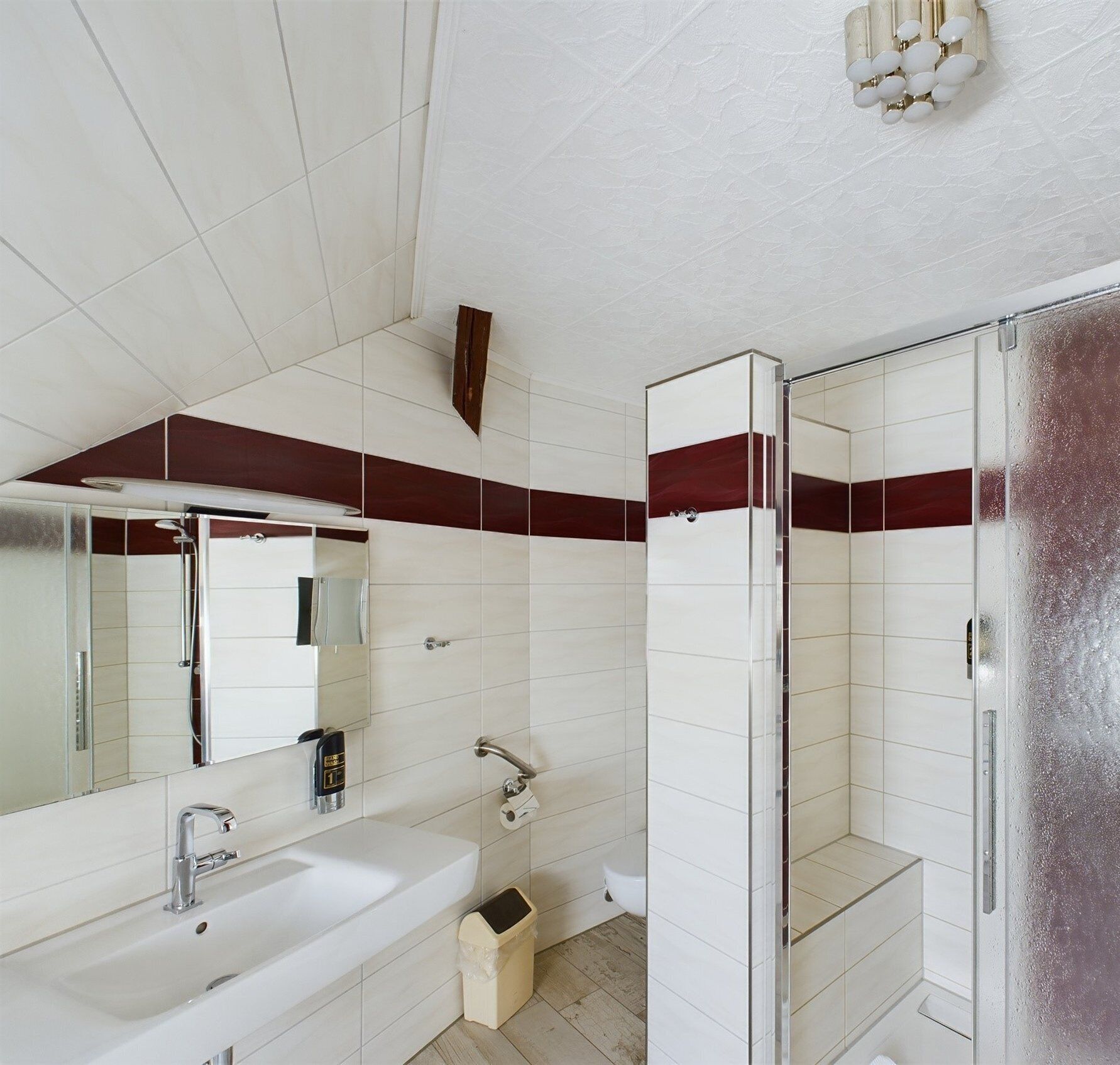 Un baño moderno con un espejo grande, un lavabo blanco, una ducha y un inodoro.