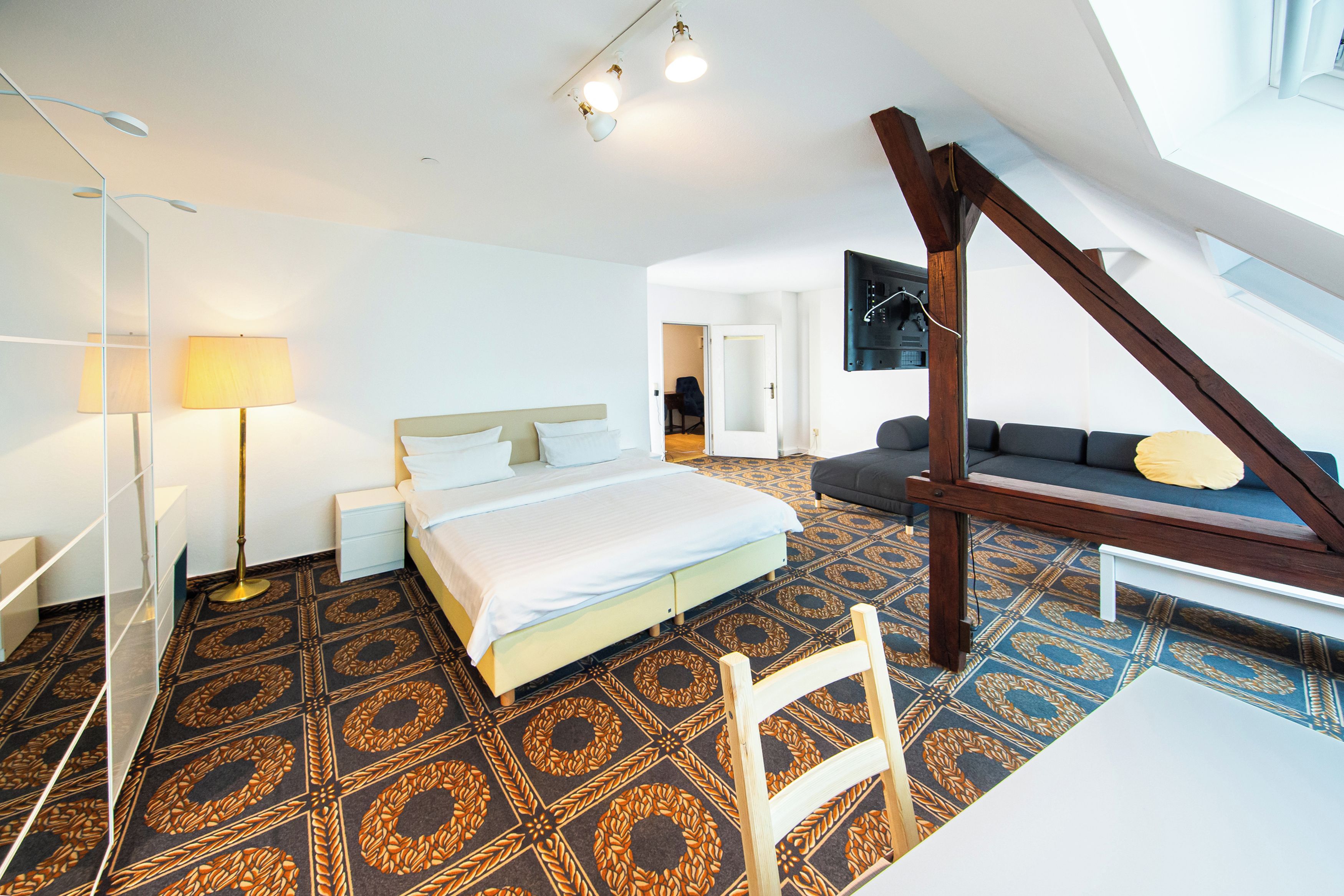 A hotel room with a bed, a sofa, a desk, and a chair. There is a staircase leading to an upper level.