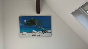 Een hotelkamer met twee bedden, een nachtkastje, een schilderij van een boom aan zee en een schuine plafond.