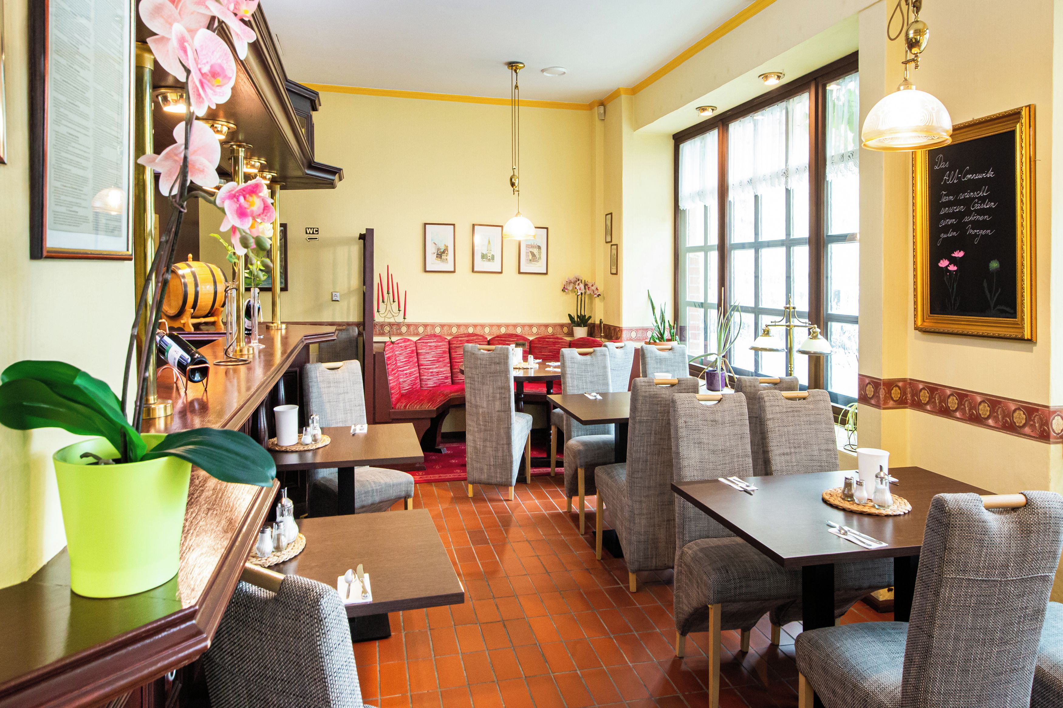 Interior de un restaurante con mesas, sillas, una zona de bar y un ventanal con luz natural.