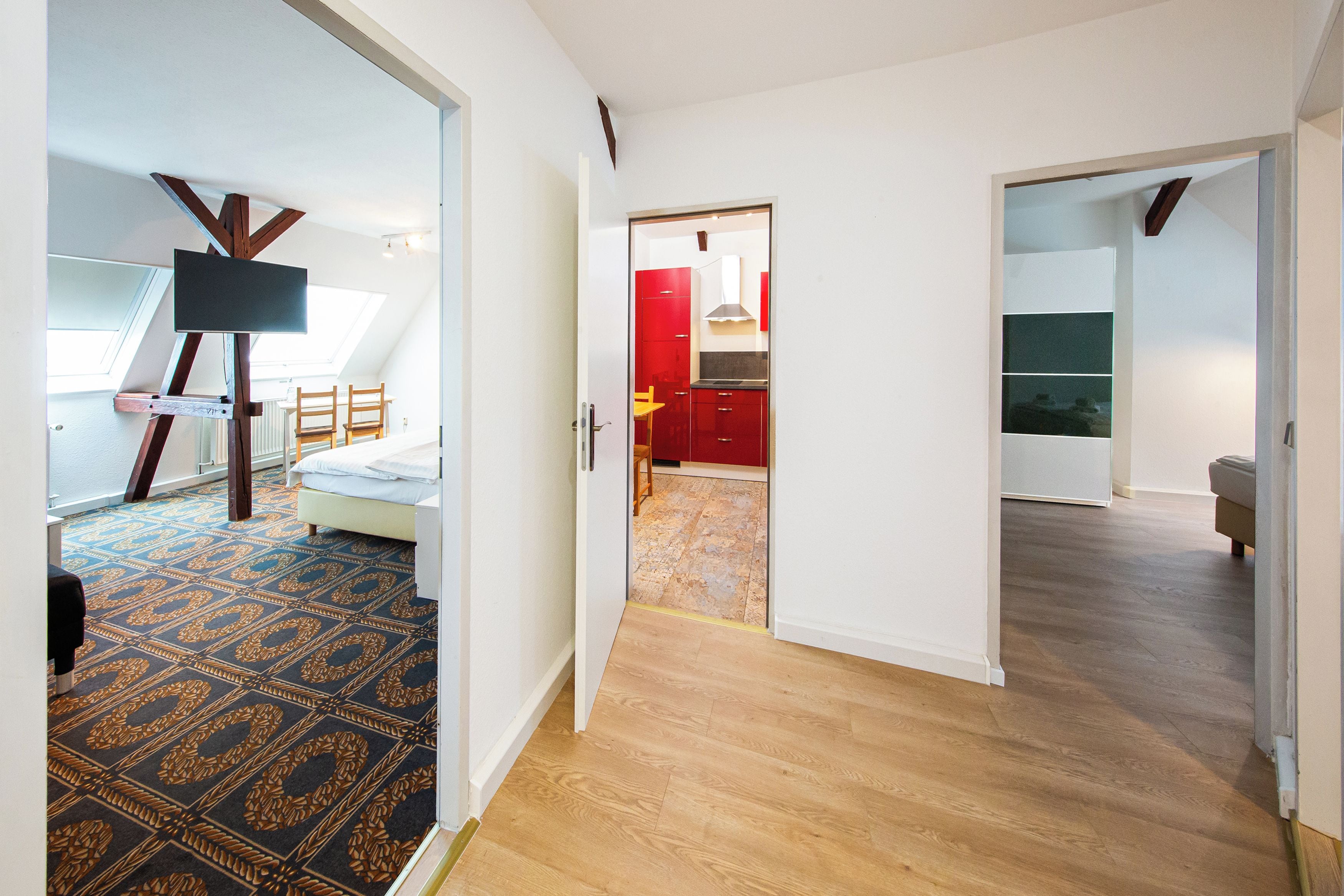 A modern interior with a patterned carpet, a bed, a dining area, and a kitchen with red cabinets.