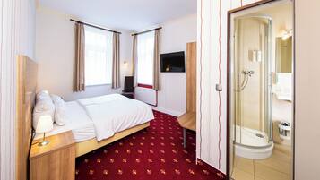 A hotel room with a bed, bedside table, lamp, TV, and a shower area.