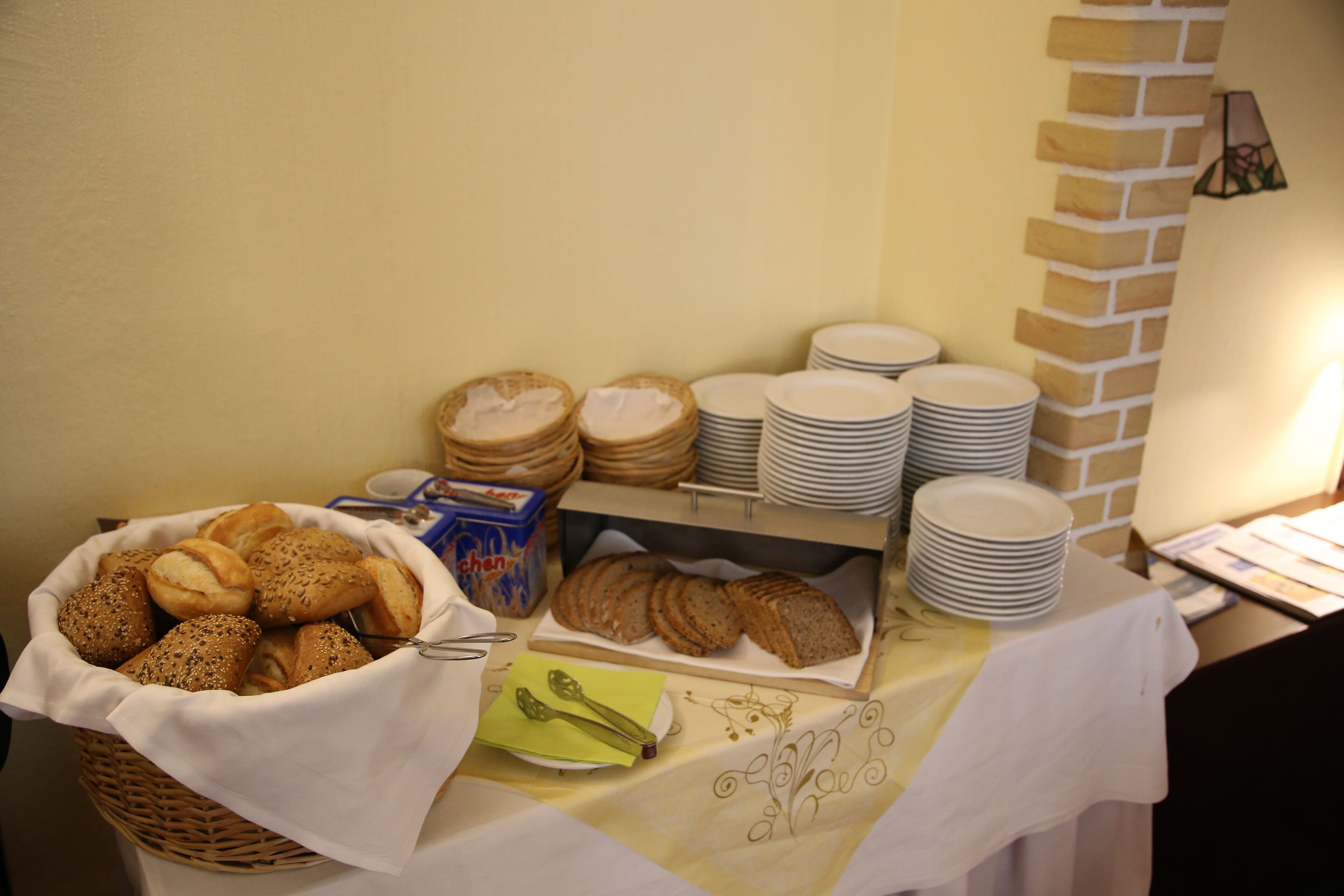 Une table de buffet avec divers pains et petits pains, des assiettes et un panier de pain.