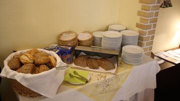 Une table de buffet avec divers pains et petits pains, des assiettes et un panier de pain.