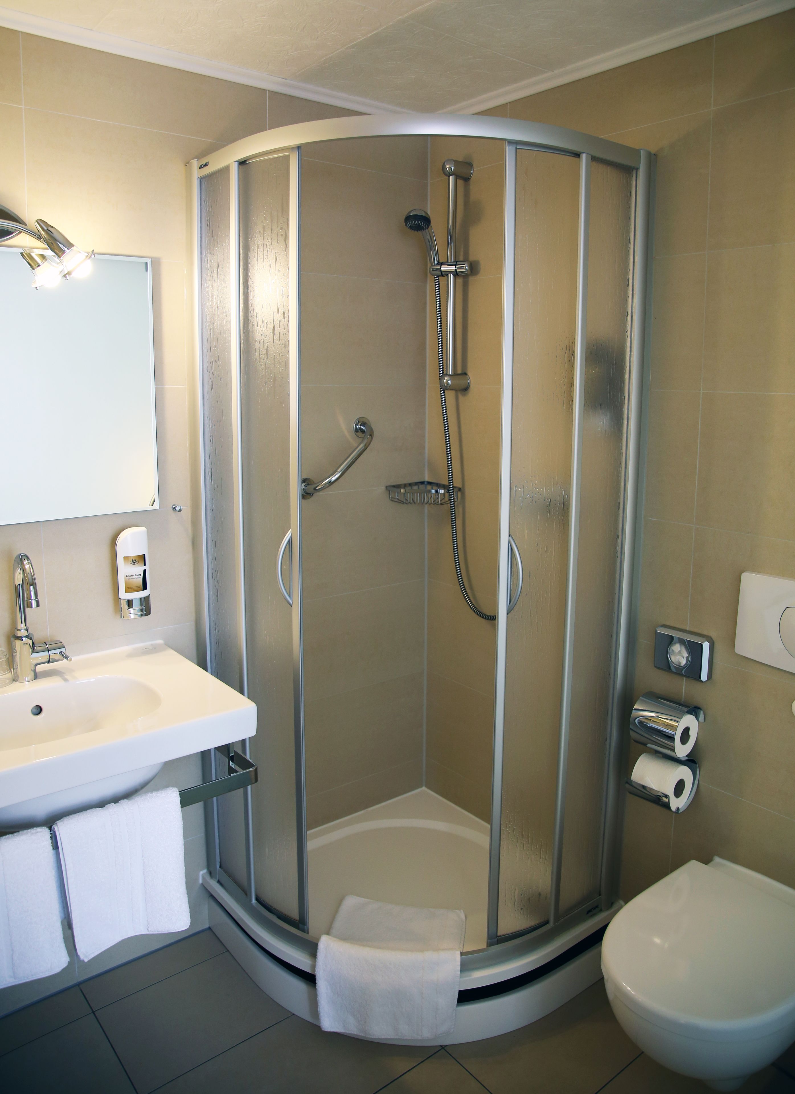 Et moderne badeværelse med bruseniche, håndvask med spejl og toilet.