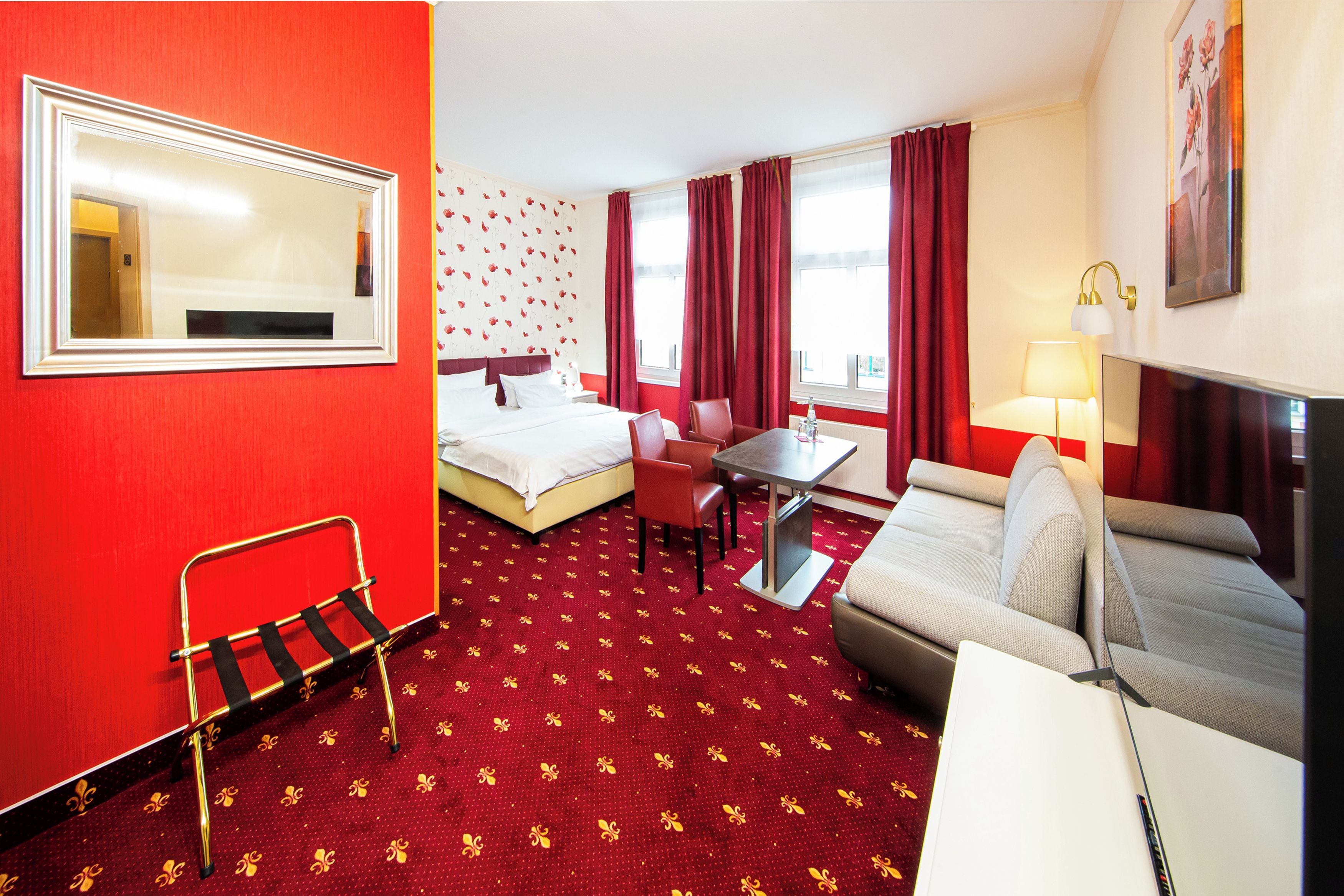 A hotel room with a bed, a desk, a chair, a sofa, a table, a lamp, and a mirror.