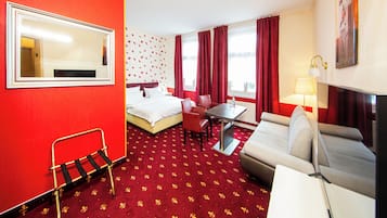 A hotel room with a bed, a desk, a chair, a sofa, a table, a lamp, and a mirror.
