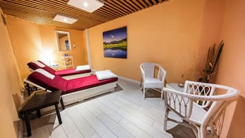 A room with two beds, a chair, a table, and a painting on the wall.