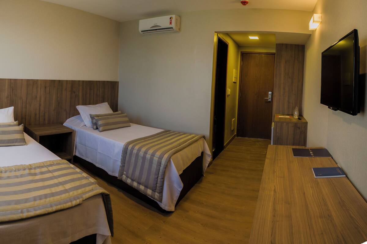 A hotel room with two single beds, a wooden headboard, a flat-screen TV, and a wooden floor.