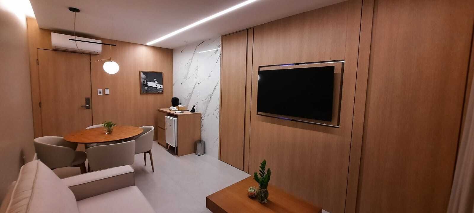 A modern living room with a round wooden table, a sofa, a TV mounted on the wall, and a small cabinet.