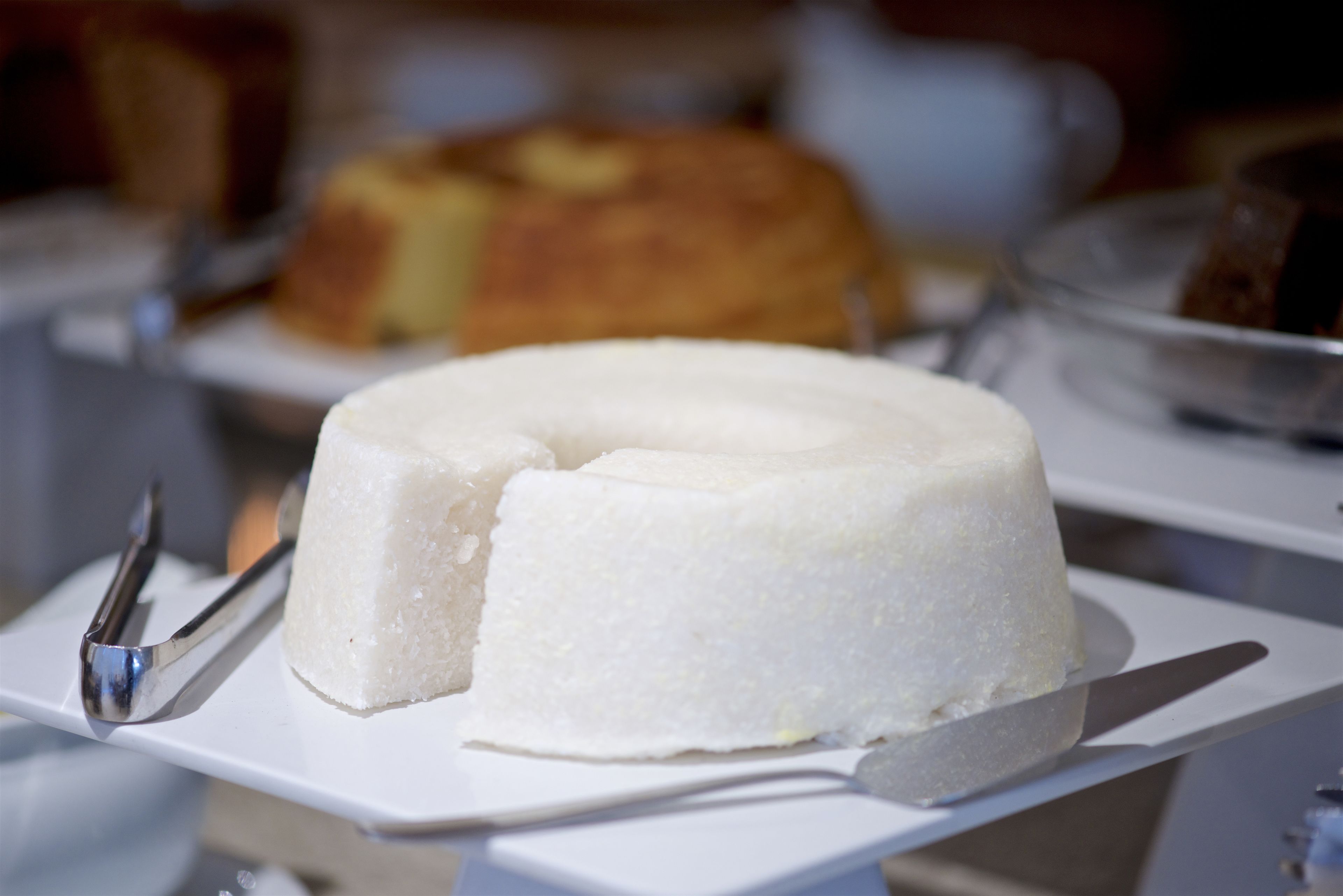 A white cake on a white plate with a knife and tongs beside it.